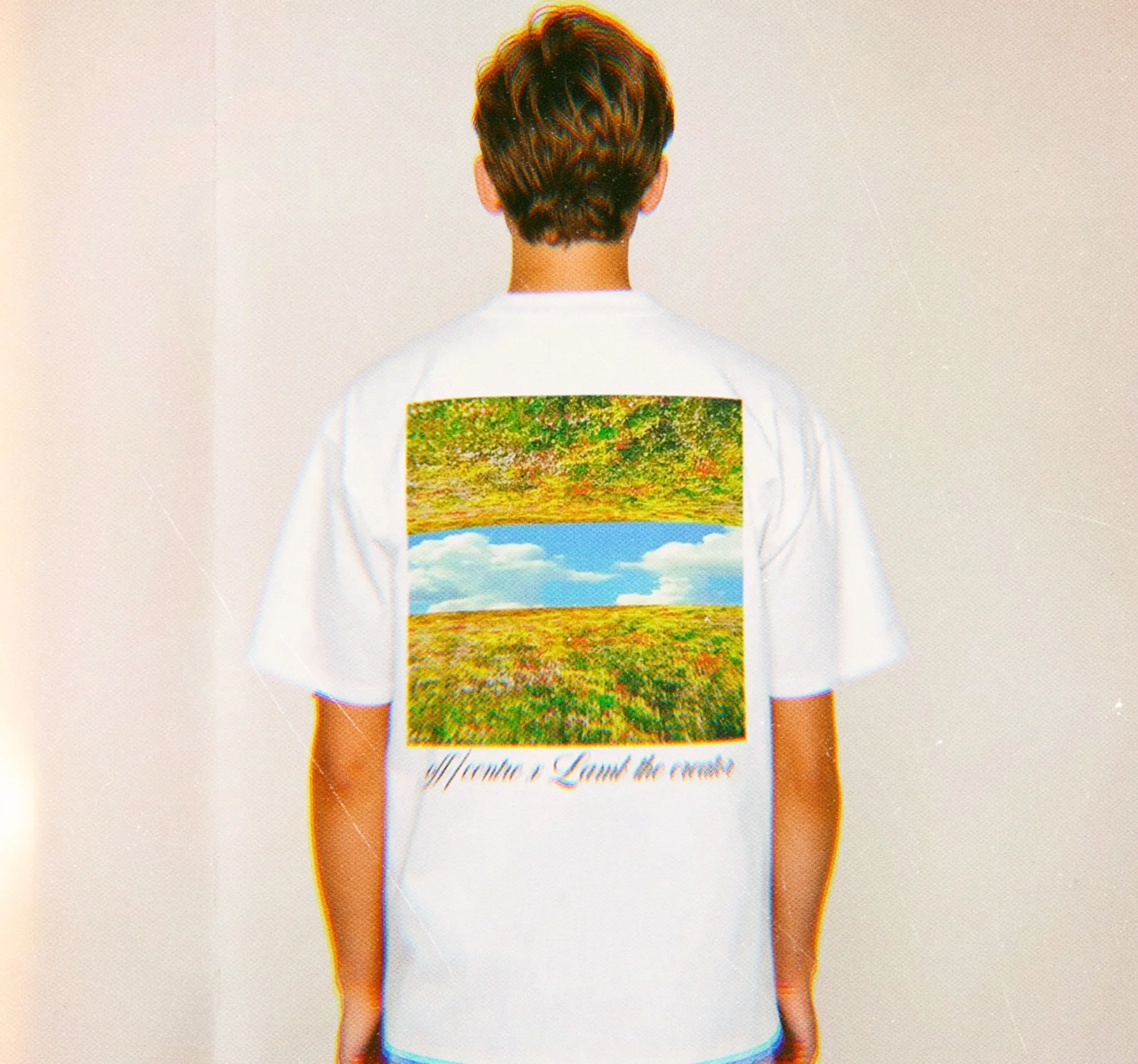 A person wearing a white t-shirt featuring a landscape design on the back, showcasing a colorful field and blue sky.