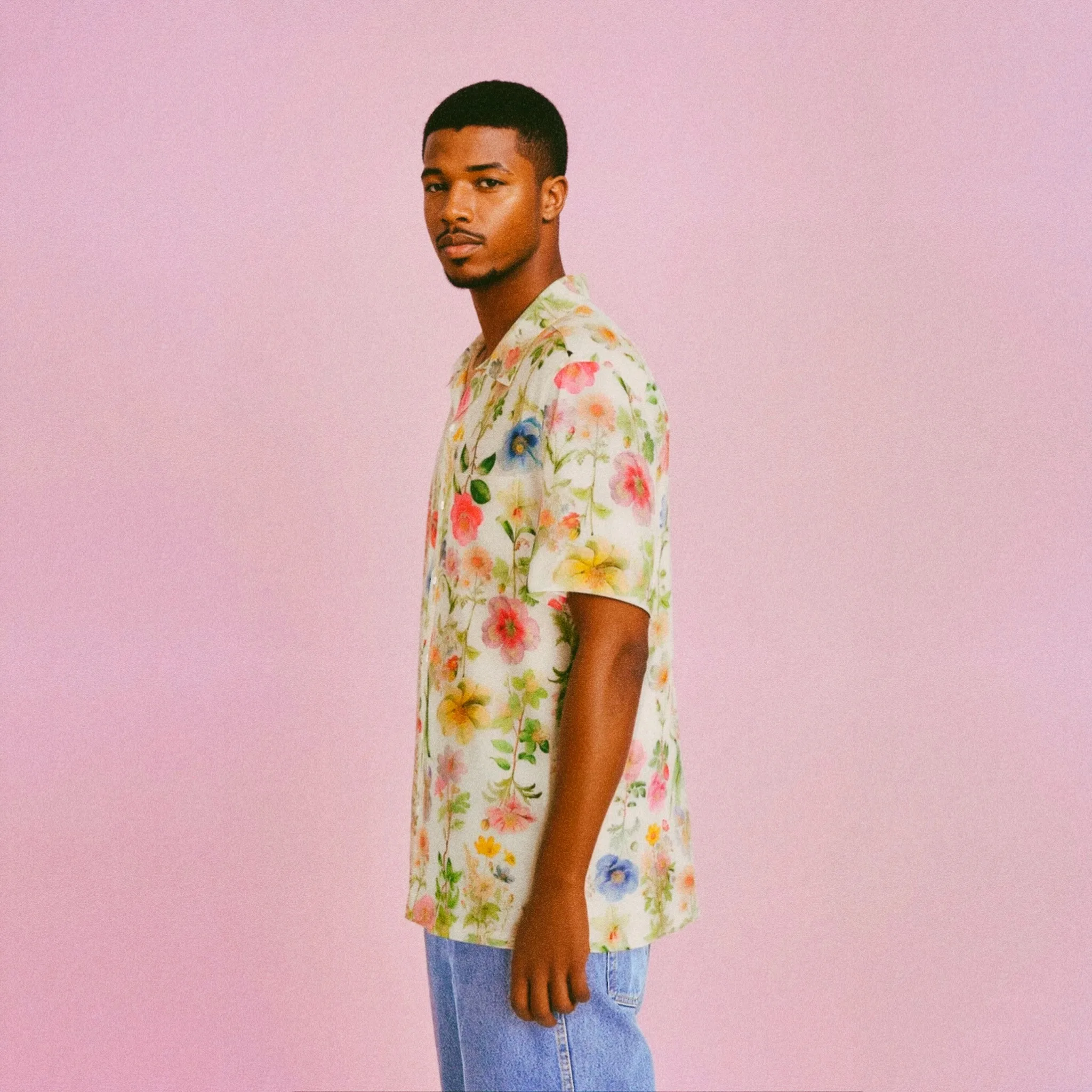 A man wearing a colorful floral shirt stands against a pink background.