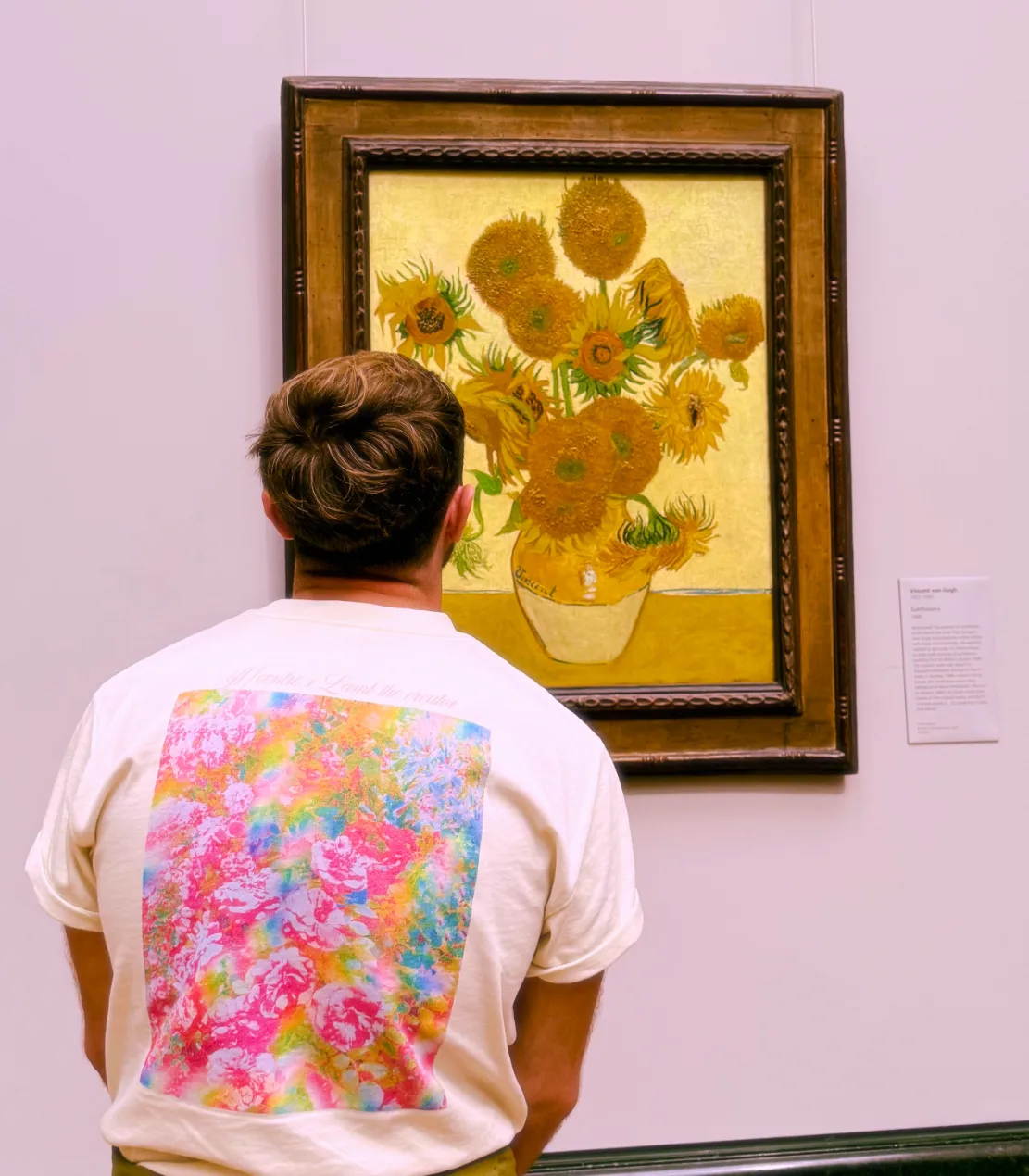 A person wearing "ethereal rosebush" tee is admiring Van Gogh's 'Sunflowers' painting in an art gallery.